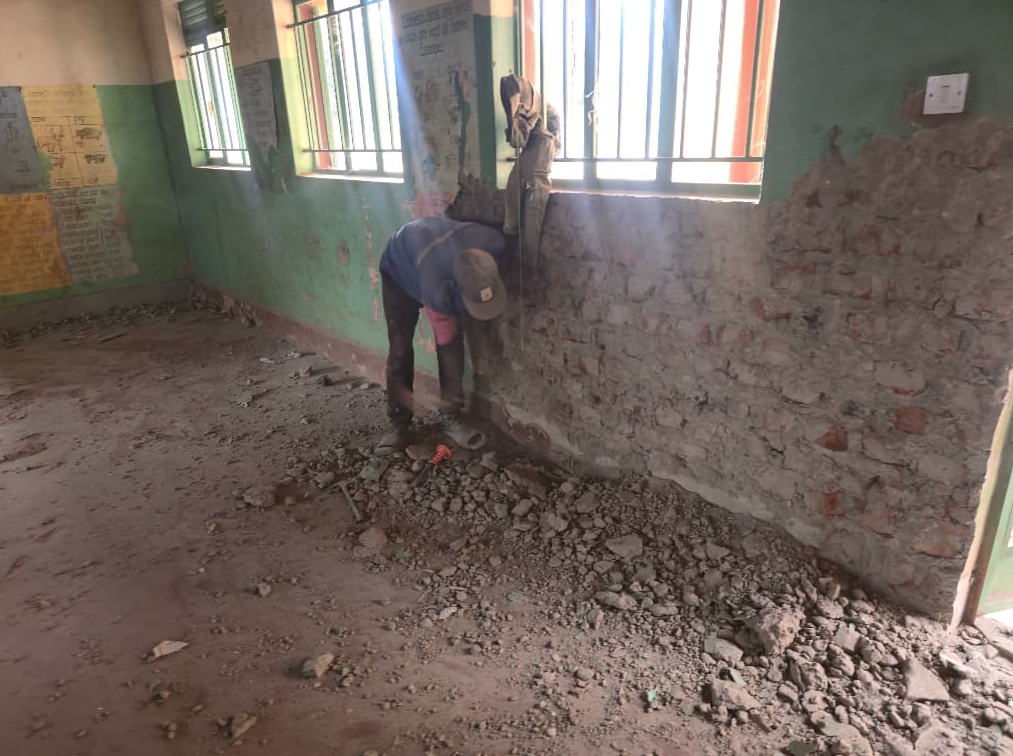 Worker repairing the interior wall of a rural Ugandan classroom